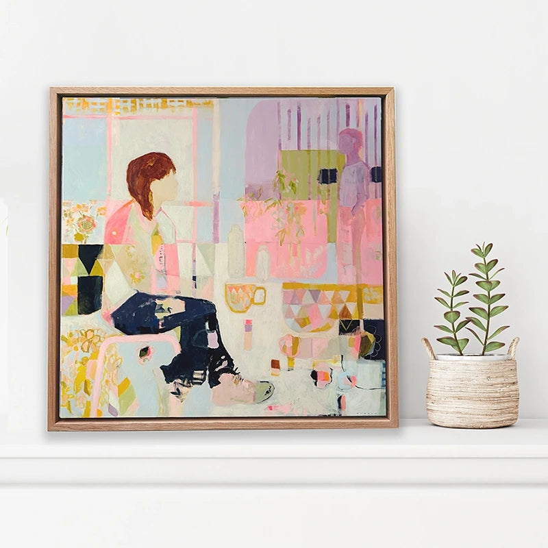 Small framed abstract art depicting a café scene in pinks and purples positioned on cabinet top next to a plant